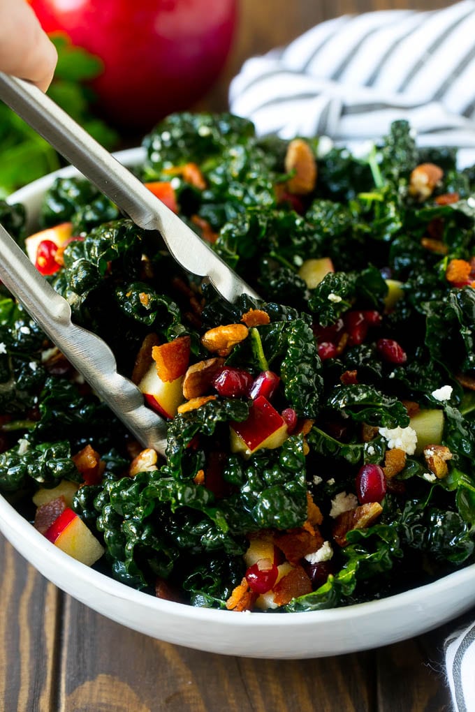 Apple Kale Salad Recipe | Kale Recipe | Fall Salad #kale #apples #bacon #salad #feta #dinner #lunch #bajap Tongs in a bowl of kale and apple salad.