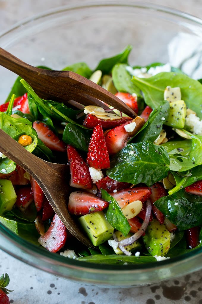 Strawberry Spinach Salad Recipe | Strawberry Salad | Spinach Salad #spinach #salad #strawberries #avocado #bajap Salad tongs in a bowl of spinach salad with strawberries.