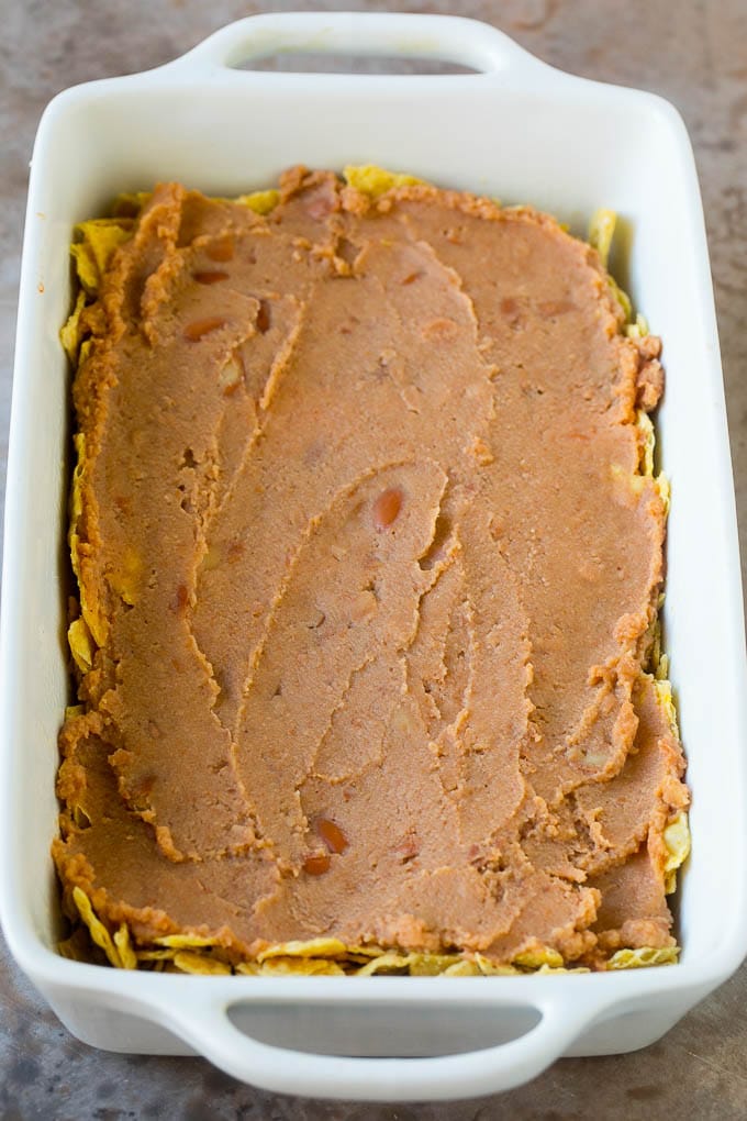 Taco Casserole Recipe | Mexican Casserole | Beef Casserole #casserole #tacos #beef #dinner #cheese #bajap A layer of refried beans on top of a crushed tortilla chips.