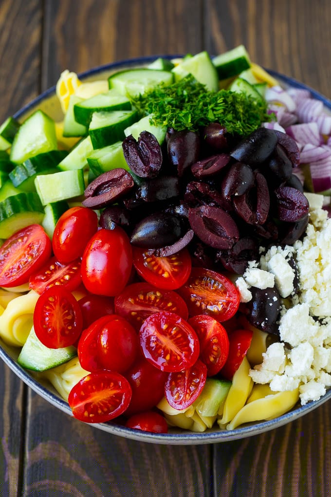 Greek Tortellini Salad Recipe | Pasta Salad | Tortellini Salad | Greek Salad #greek #tortellini #pasta #salad #cucumbers #olives #dinner #bajap Tortellini in a bowl topped with olives, tomatoes, cucumber and feta cheese.