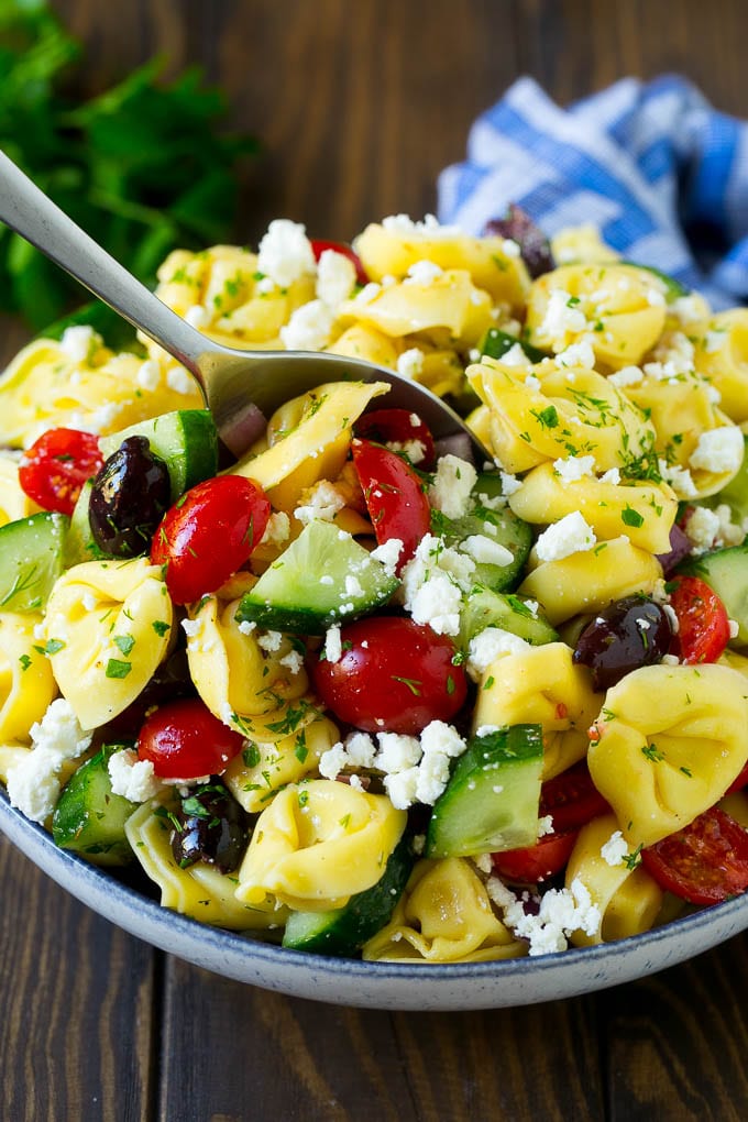 Greek Tortellini Salad Recipe | Pasta Salad | Tortellini Salad | Greek Salad #greek #tortellini #pasta #salad #cucumbers #olives #dinner #bajap A bowl of Greek tortellini salad with a serving spoon in it.