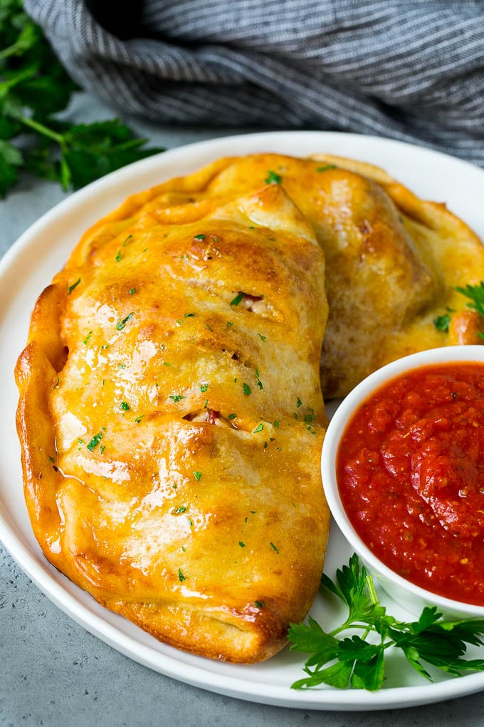 Calzone Recipe | Pizza Pockets #pizza #calzone #pepperoni #sausage #peppers #dinner #bajap #cheese A homemade calzone served with pizza sauce.