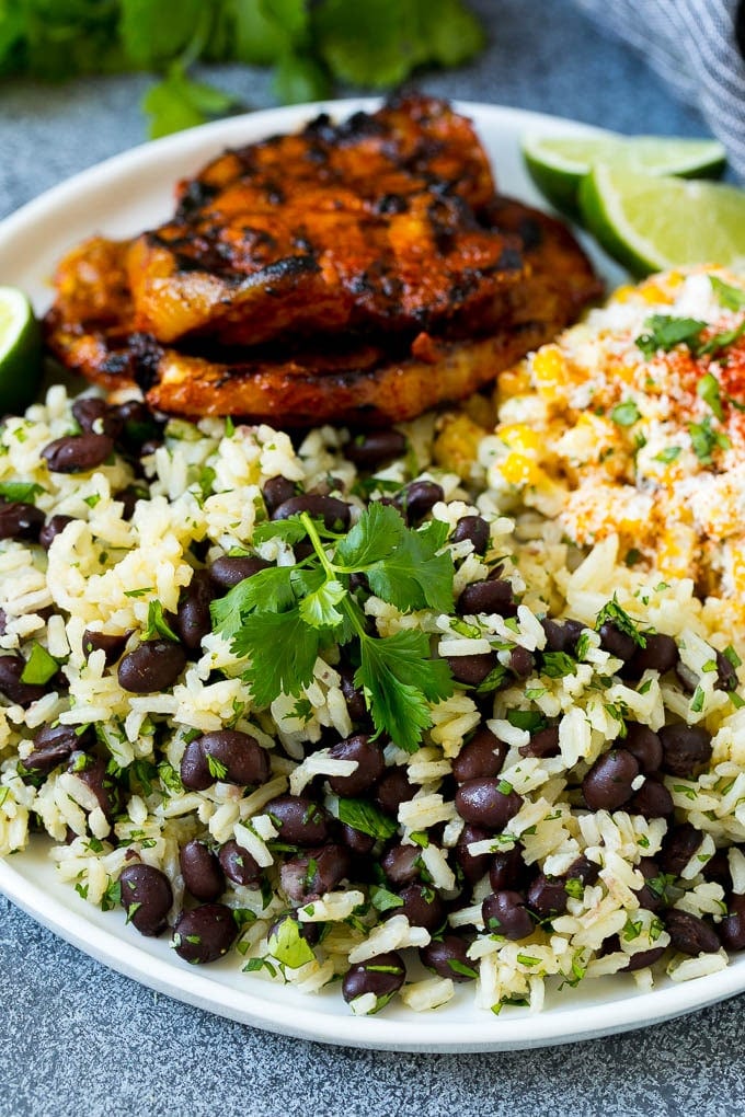 Black Beans and Rice Recipe | Cuban Black Beans | Beans and Rice #beans #rice #blackbeans #sidedish #glutenfree #dinner #bajap A plate of black beans and rice with grilled pork and Mexican corn.