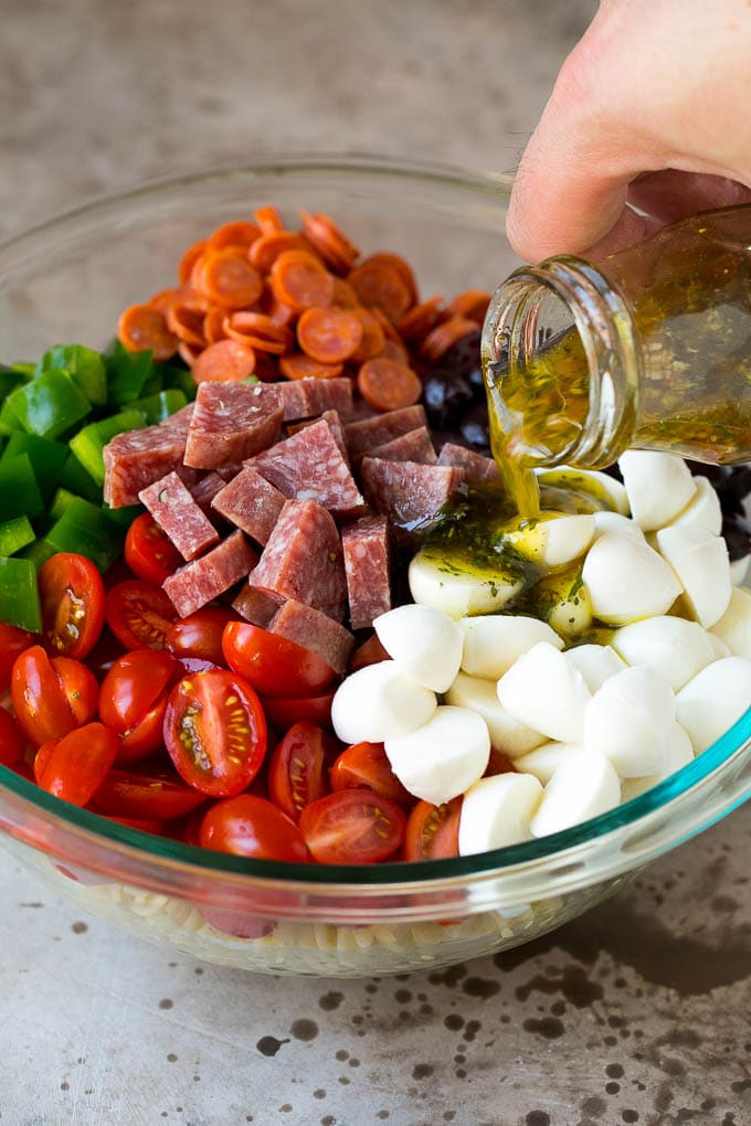 Italian Pasta Salad | Pasta Salad Recipe #pasta #salad #pastasalad #pepperoni #salami #olives #cheese #sidedish #bajap Italian dressing being poured over pasta salad ingredients.