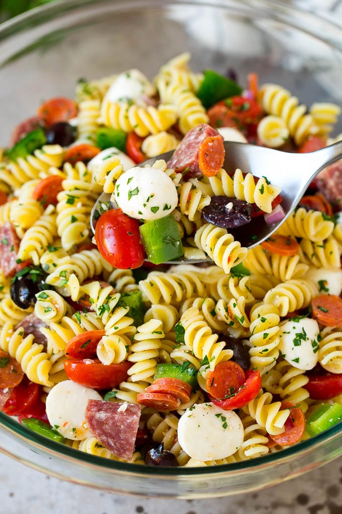 Italian Pasta Salad | Pasta Salad Recipe #pasta #salad #pastasalad #pepperoni #salami #olives #cheese #sidedish #bajap A serving spoon in a bowl of Italian style pasta salad.