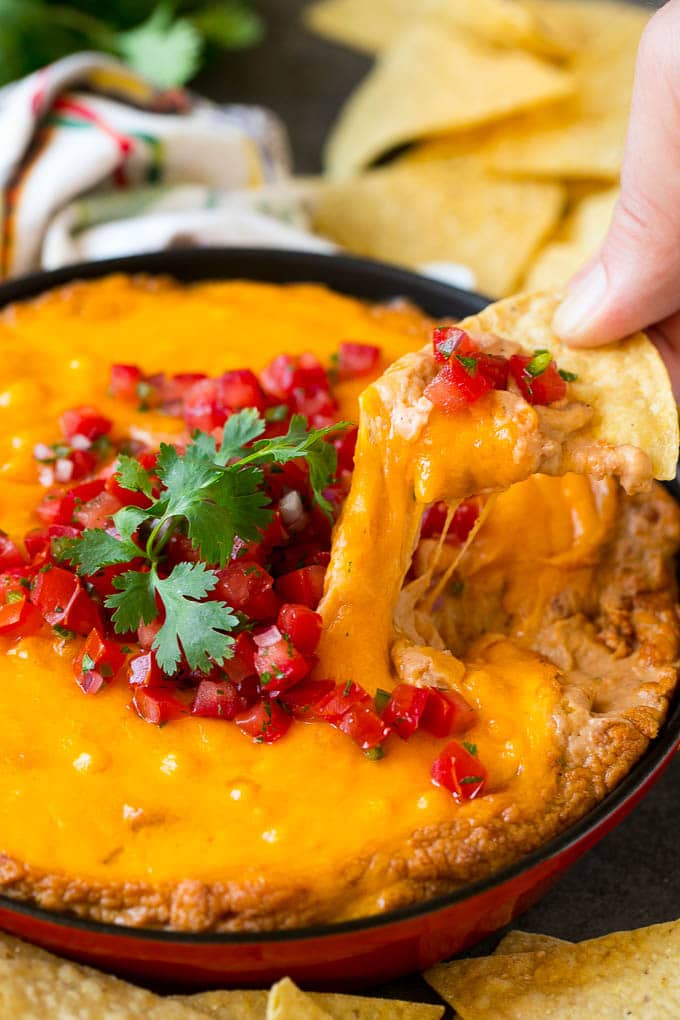 Bean Dip Recipe | Mexican Dip #dip #appetizer #mexicanfood #beans #cheese #bajap A tortilla chip scooping out a serving of Mexican bean dip.