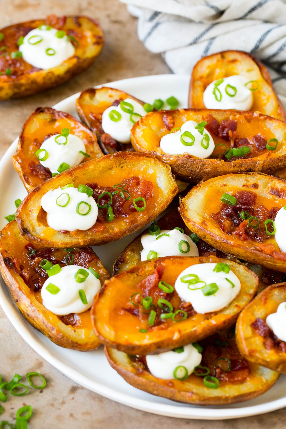 Potato Skins Recipe | Loaded Potatoes #potatoes #appetizer #snack #cheese #bacon #bajap A serving plate of potato skins topped with bacon and sour cream.