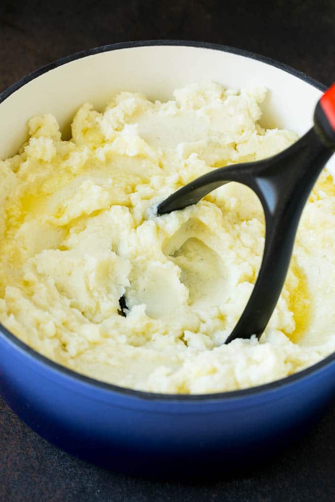 Garlic Mashed Potatoes Recipe #garlic #potatoes #mashedpotatoes #sidedish #dinner #thanksgiving #bajap A potato masher smashing diced cooked potatoes.