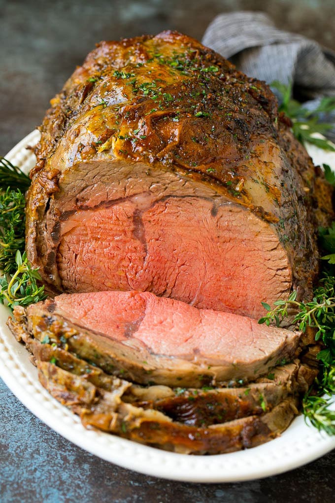 Prime Rib Recipe #primerib #beef #roast #dinner #thanksgiving #christmas #keto #lowcarb #bajap A sliced slow roasted prime rib roast surrounded by fresh herbs.