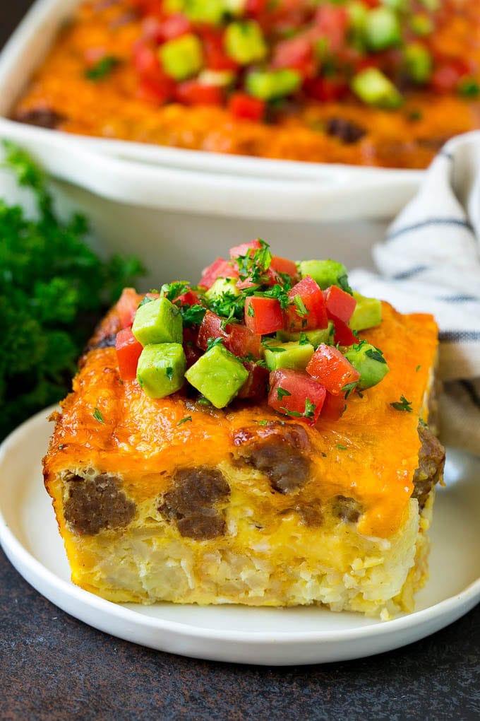 Sausage Egg Casserole Recipe | Egg Casserole #eggs #sausage #potato #cheese #casserole #breakfast #brunch #bajap A slice of sausage egg casserole with a garnish of fresh tomatoes.