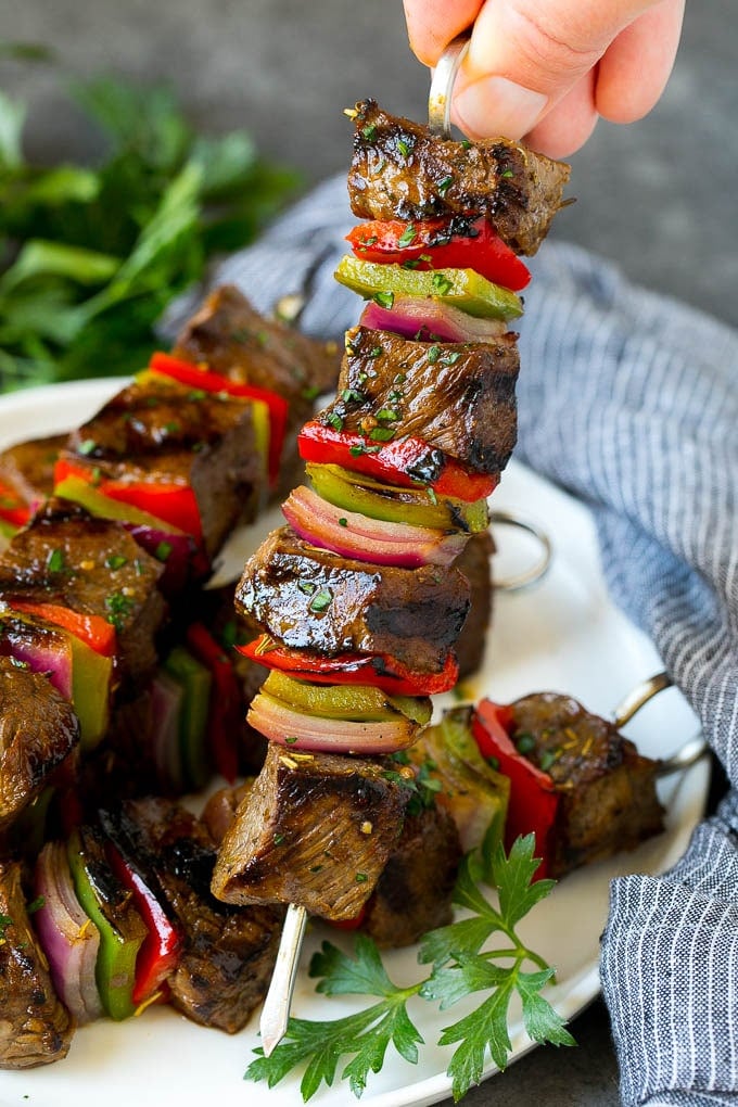 Beef Shish Kabobs Recipe | Beef Kabobs #grilling #beef #steak #dinner #bajap #peppers A hand holding a beef shish kabob with peppers and onions.