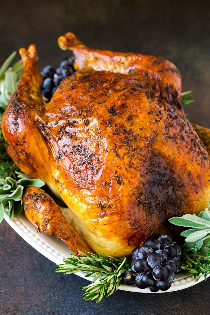 Thanksgiving Turkey Recipe | Roasted Turkey #turkey #thanksgiving #fall #dinner #bajap A whole roasted Thanksgiving turkey on a platter that's decorated with grapes and herbs.