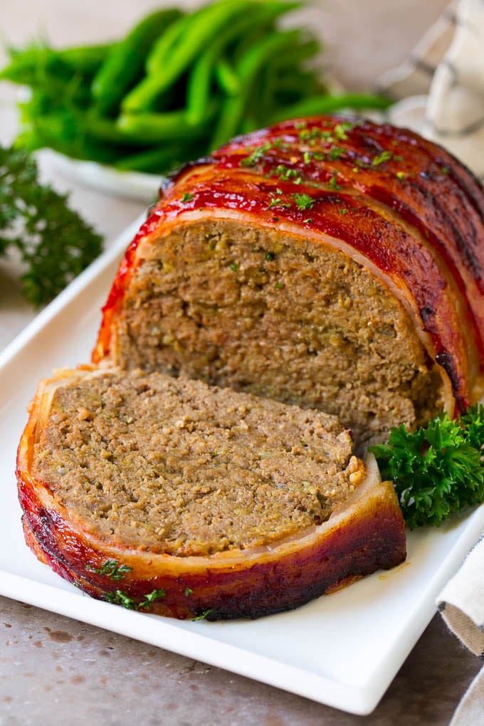 Bacon Wrapped Meatloaf Recipe | Beef Meatloaf #meatloaf #beef #groundbeef #bacon #dinner #bajap A bacon wrapped meatloaf with a slice out of it, on a serving platter.