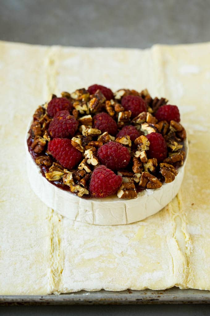 Baked Brie Recipe | Pastry Wrapped Brie #brie #cheese #appetizer #pecans #raspberries #bajap A wheel of cheese topped with jam, raspberries and pecans.
