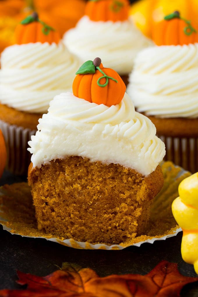 Pumpkin Cupcakes Recipe | Pumpkin Cake #cake #cupcakes #pumpkin #frosting #baking #fall #thanksgiving #bajap A pumpkin cupcake cut in half, surrounded by fall decorations.