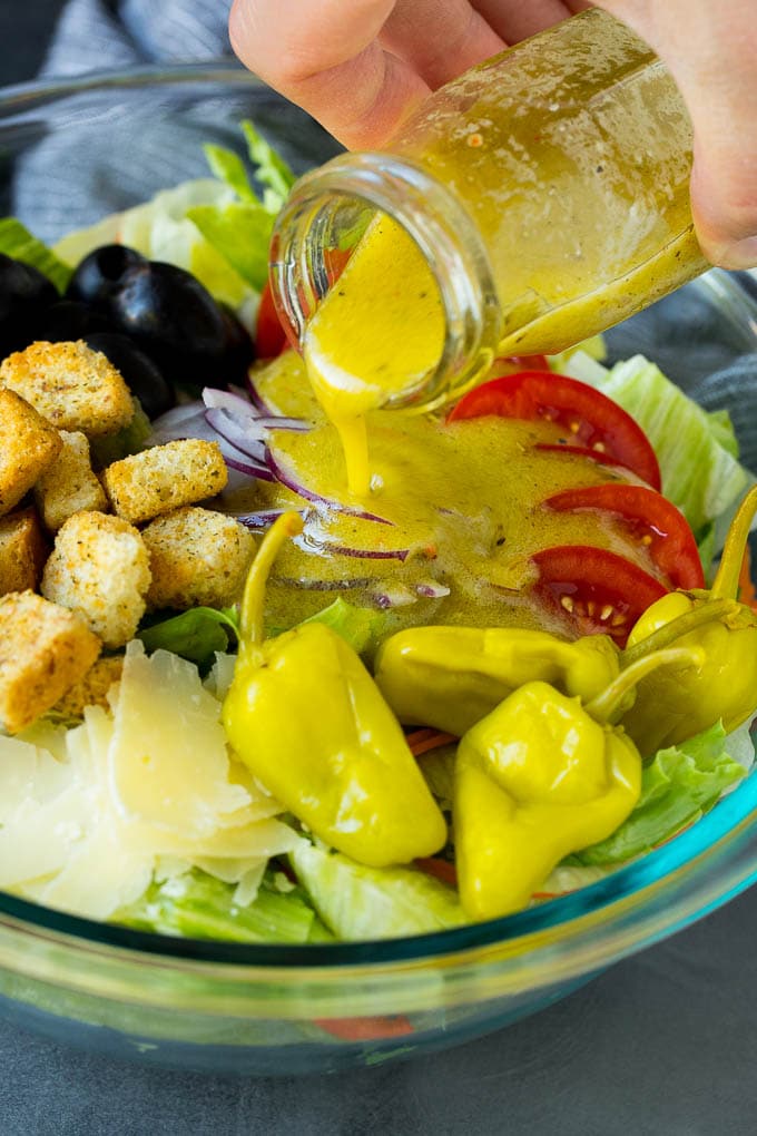 Olive Garden Salad Recipe | Italian Salad #salad #lettuce #olives #sidedish #dinner #bajap Dressing being poured over a bowl of salad.