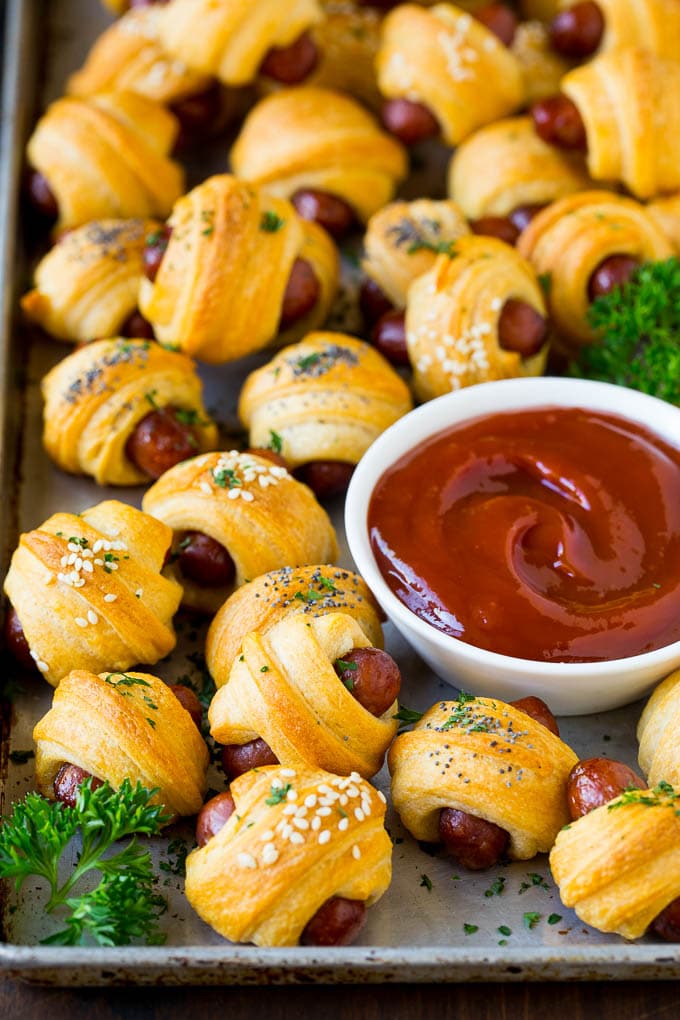 Pigs in a Blanket Recipe #hotdogs #appetizer #snack #comfortfood #bajap A sheet pan of pigs in a blanket, garnished with parsley and served with ketchup.