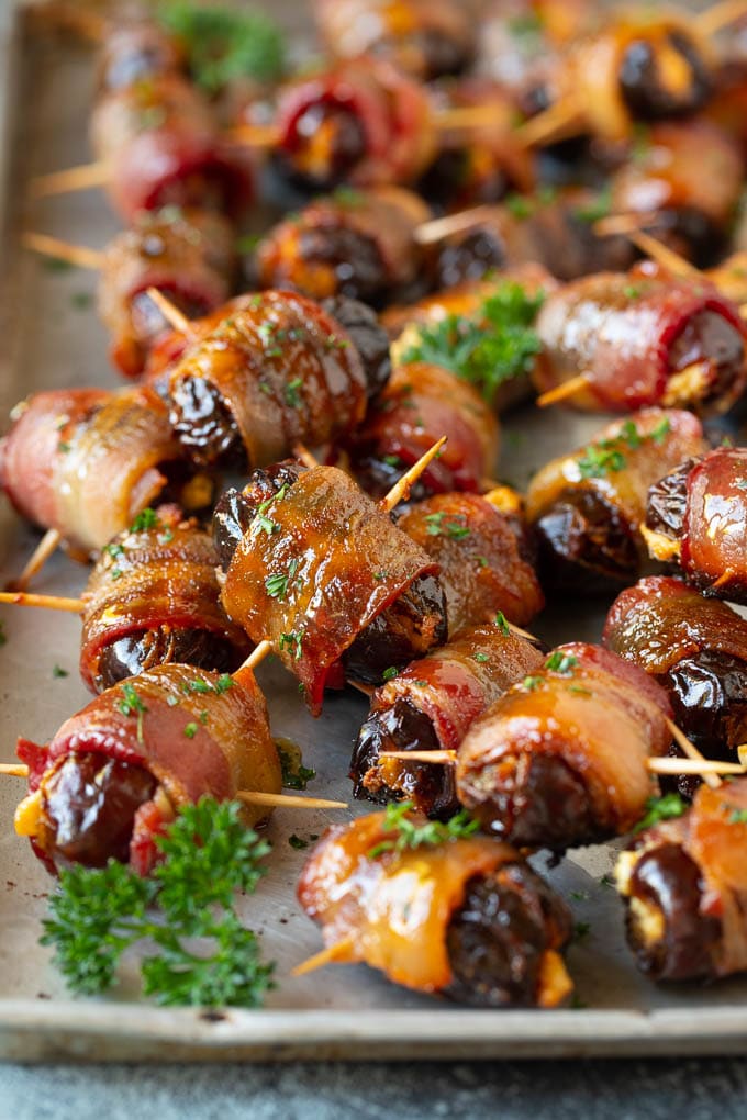 Bacon Wrapped Dates #appetizer #bacon #dates #cheese #bajap Bacon wrapped dates on a sheet pan garnished with parsley.