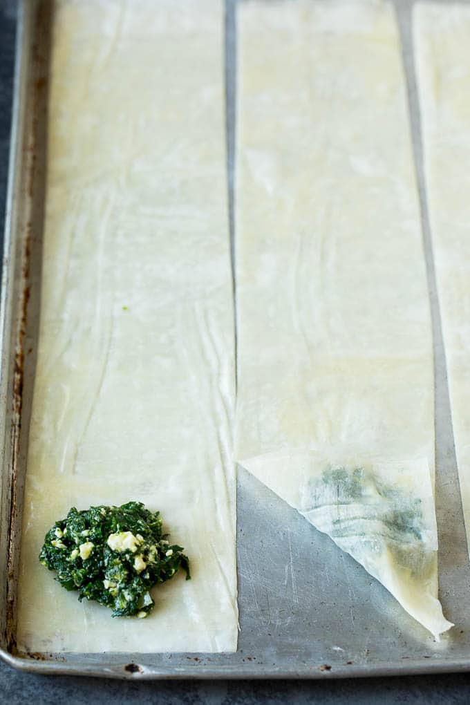 Spanakopita Recipe #appetizer #snack #spinach #cheese #bajap Strips of phyllo dough with spoonfuls of filling on top.