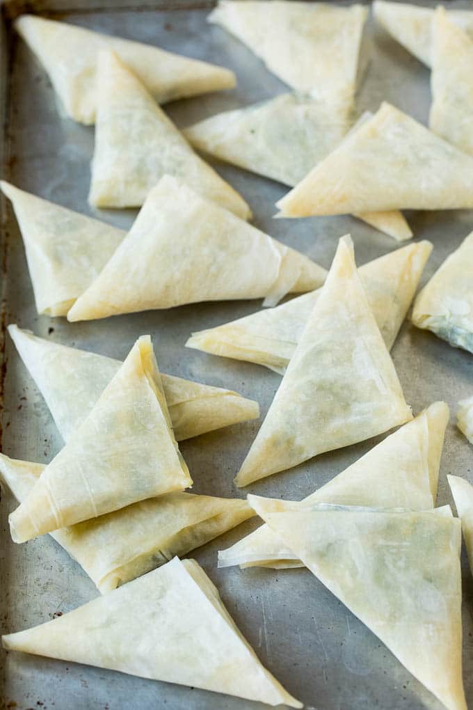 Spanakopita Recipe #appetizer #snack #spinach #cheese #bajap Folded stuffed phyllo triangles on a sheet pan.