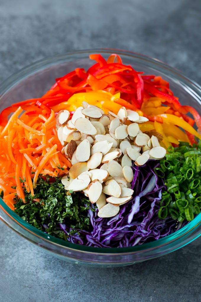 Asian Slaw Recipe #salad #slaw #sidedish #bajap Shredded cabbage, vegetables and almonds in a bowl.