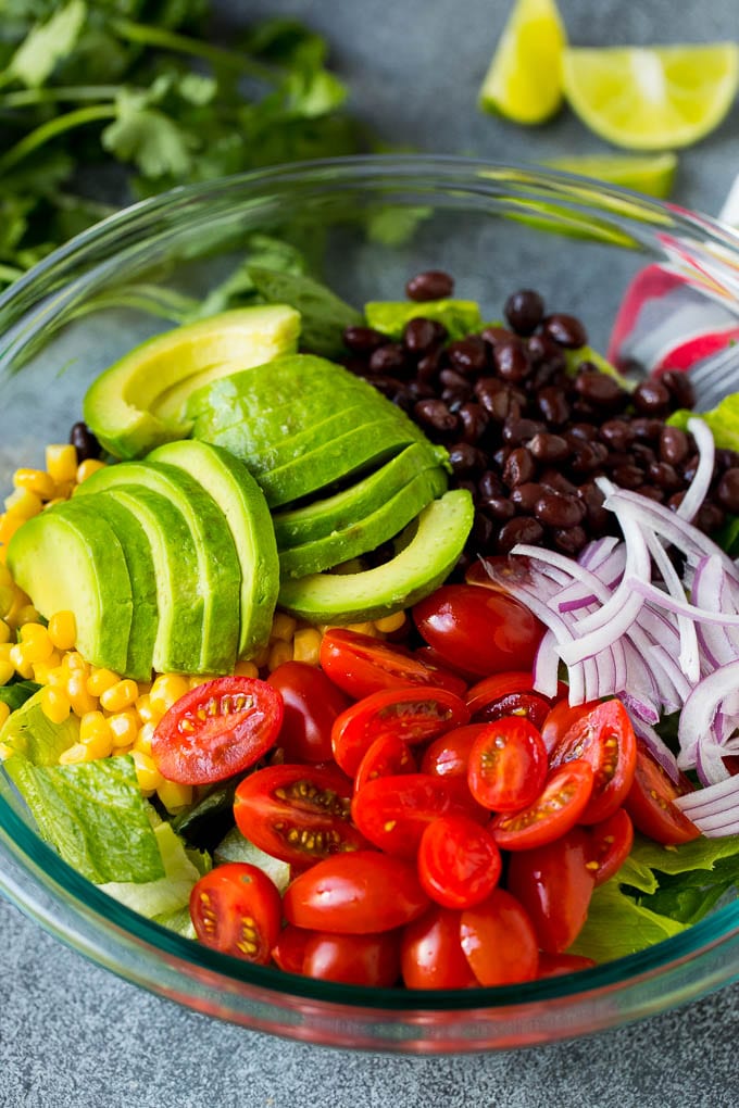 Mexican Salad Recipe #salad #corn #beans #avocado #tomatoes #bajap Lettuce, tomatoes, onion, corn, avocado and black beans in a bowl.