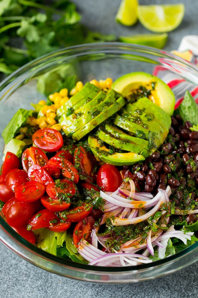Mexican Salad Recipe #salad #corn #beans #avocado #tomatoes #bajap Dressing poured over a bowl of lettuce, tomatoes, avocado and beans.