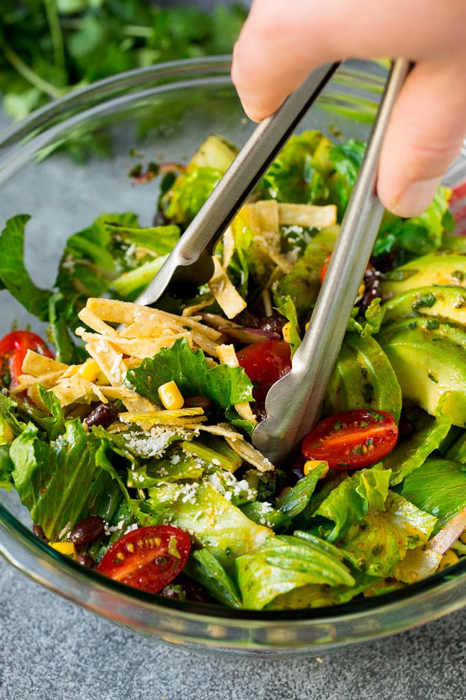 Mexican Salad Recipe #salad #corn #beans #avocado #tomatoes #bajap Tongs serving up a portion of Mexican salad.