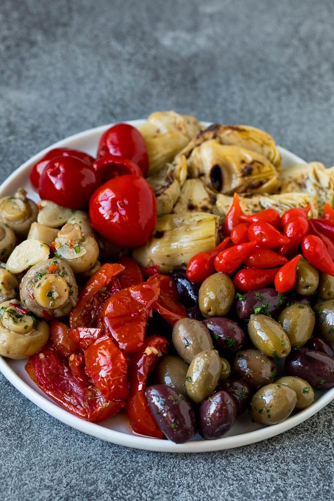 This mezze platter is filled with Mediterranean delicacies including dolmas, hummus, vegetables, pita bread and salads. #appetizer #bajap A plate of olives, peppers and grilled artichokes.