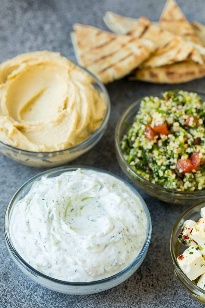 This mezze platter is filled with Mediterranean delicacies including dolmas, hummus, vegetables, pita bread and salads. #appetizer #bajap Bowls of hummus, tzatziki and tabbouleh.