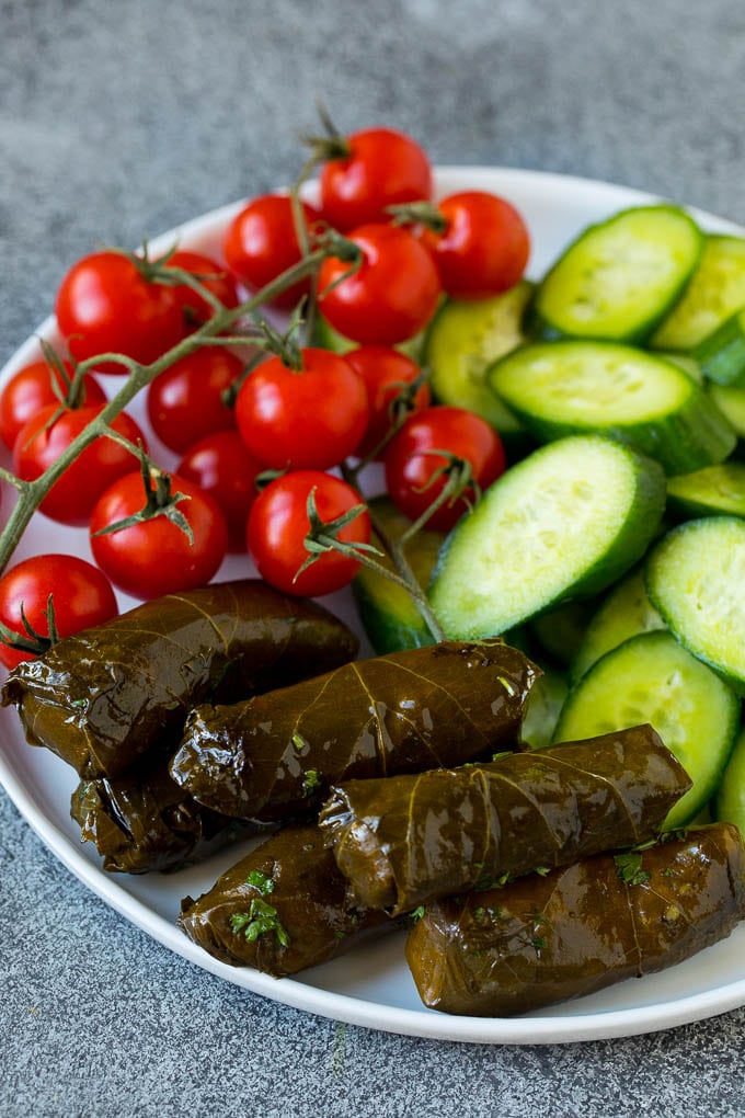 This mezze platter is filled with Mediterranean delicacies including dolmas, hummus, vegetables, pita bread and salads. #appetizer #bajap A plate of cherry tomatoes, cucumber slices and dolmas.