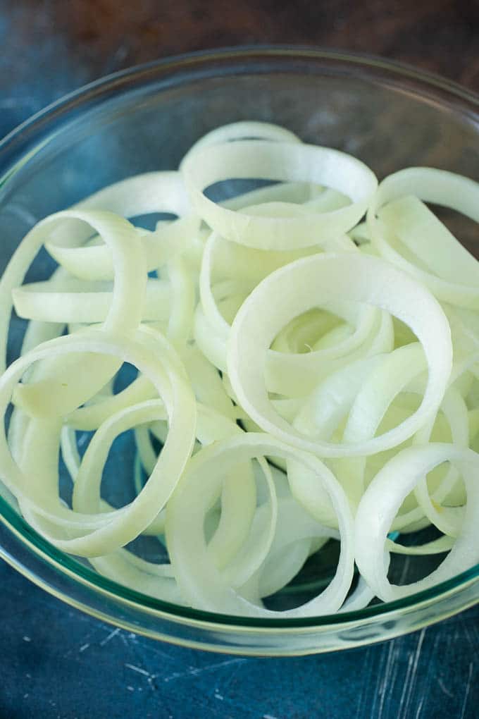 Crispy homemade onion rings that are fried in a flavorful beer batter. #onions #bajap #appetizer Raw onion slices in a bowl.