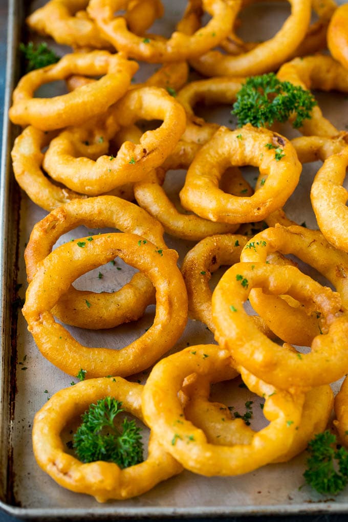 Crispy homemade onion rings that are fried in a flavorful beer batter. #onions #bajap #appetizer Beer battered onion rings on a sheet pan.