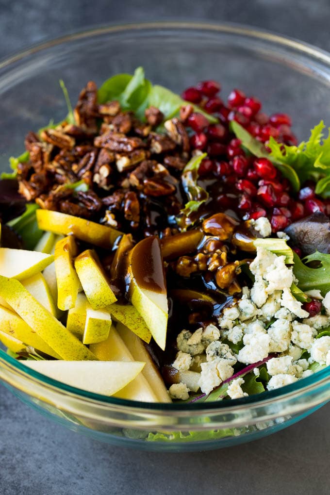 Pear Salad Recipe #salad #pears #fall #winter #dinner #bajap Balsamic dressing poured over a bowl of mixed greens, fruit and pomegranate seeds.
