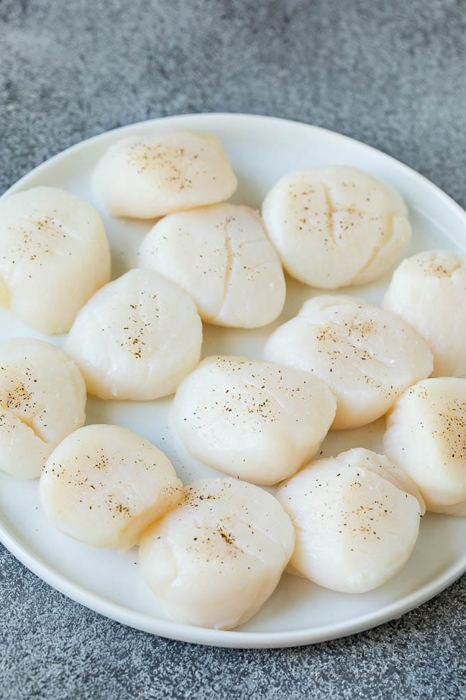 Seared scallops with a garlic and herb butter sauce. An easy and elegant dinner! #seafood #dinner #bajap Raw sea scallops on a plate.