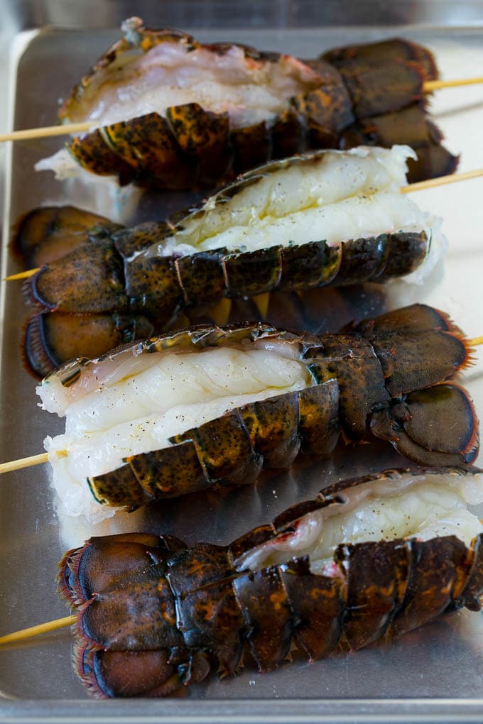 Grilled lobster tail drizzled with garlic butter is an easy and elegant dinner option. #lobster #bajap Raw lobster tails split open with skewers through them.