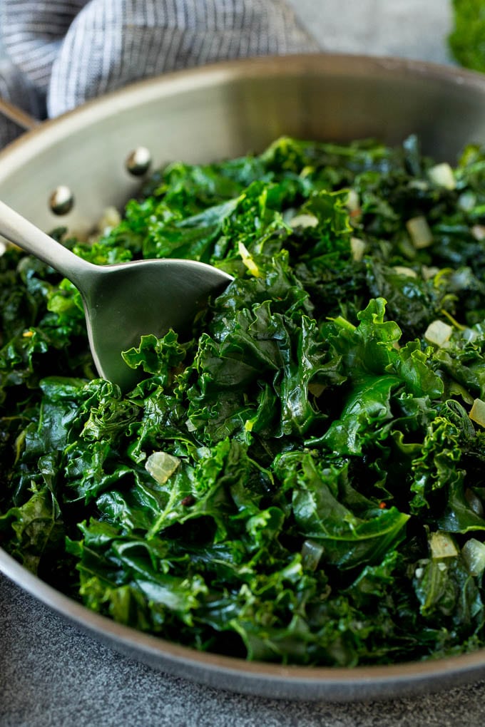 Sauteed kale flavored with olive oil and garlic, a quick and easy side dish! #kale #bajap A pan of sauteed kale with a serving spoon in it.