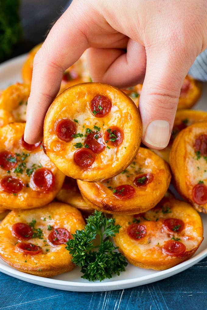 Mini pizzas topped with pepperoni are a fun and easy appetizer option. #pizza #bajap #appetizer A platter of mini pizzas with a hand reaching for one.
