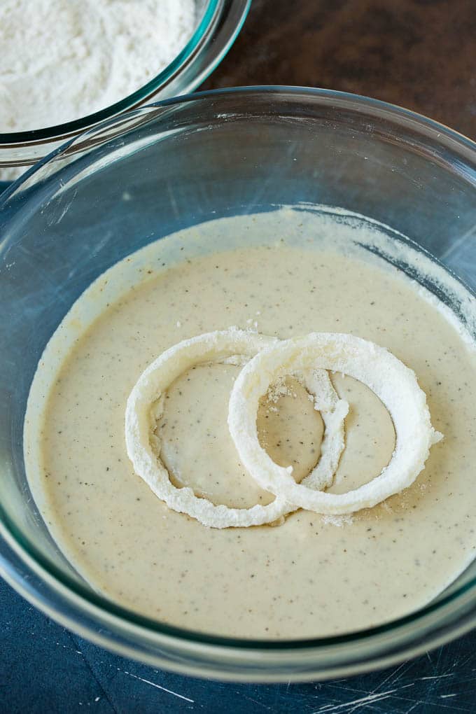 Crispy homemade onion rings that are fried in a flavorful beer batter. #onions #bajap #appetizer Floured onions in a bowl of beer batter.