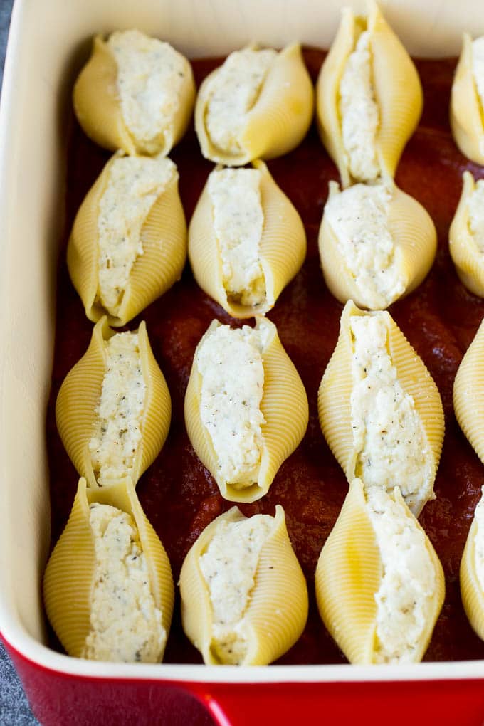 Baked stuffed shells filled with three types of cheese and topped with marinara sauce. #pasta #bajap Pasta filled with cheese on a bed of tomato sauce.