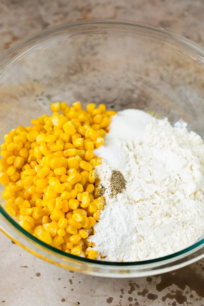 These crispy corn fritters are easy to make and are the perfect appetizer or lighter main course. #corn #bajap Flour, corn and seasonings in a mixing bowl.