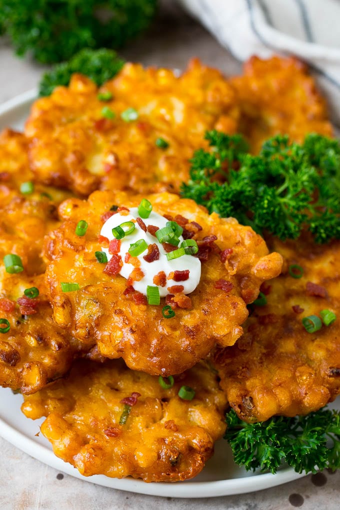 These crispy corn fritters are easy to make and are the perfect appetizer or lighter main course. #corn #bajap A plate of corn fritters garnished with parsley, and topped with sour cream.