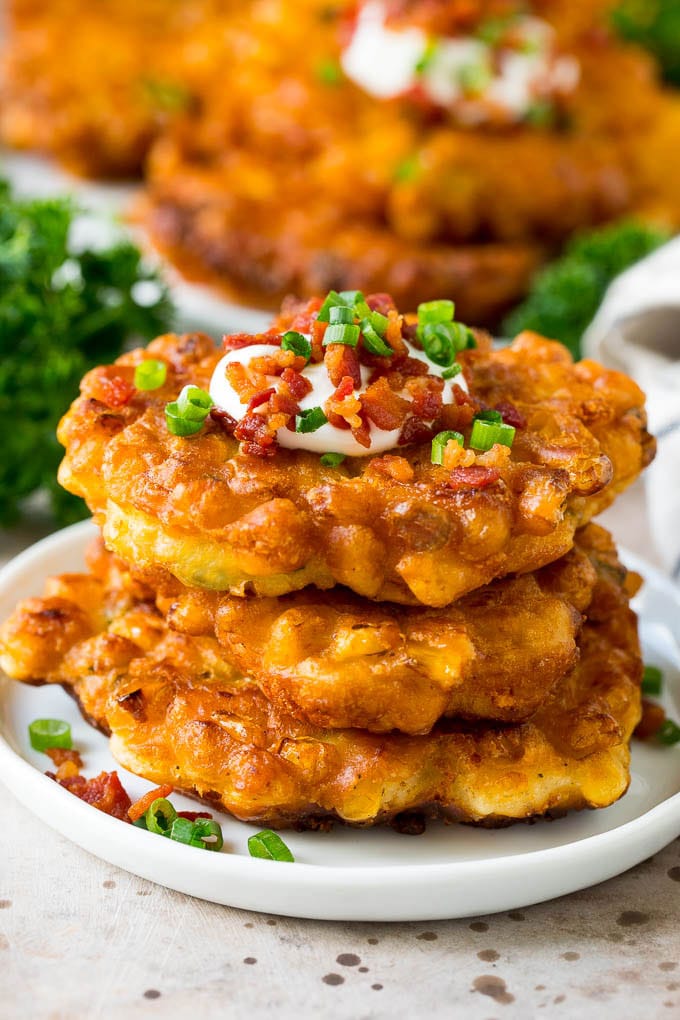 These crispy corn fritters are easy to make and are the perfect appetizer or lighter main course. #corn #bajap A stack of corn fritters topped with bacon, sour cream and green onions.