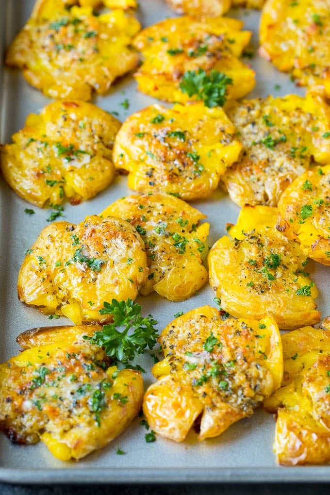 These smashed potatoes are baby potatoes that are boiled until tender, then smashed flat, topped with garlic and herb butter, and roasted until crispy and browned. Smashed potatoes on a sheet pan, topped with garlic butter and parsley.