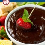 A bowl of chocolate fondue with a strawberry being dipped into it.