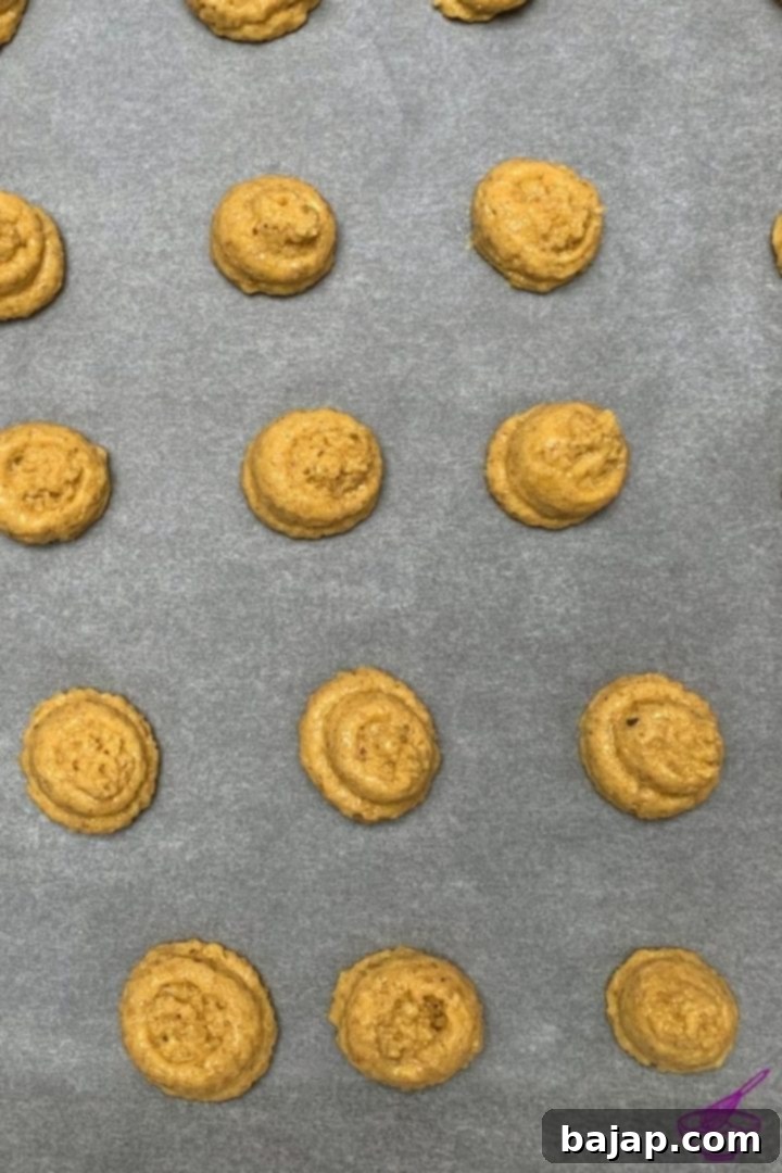 Walnut cookie dough being piped onto a baking sheet lined with parchment paper, creating small mounds ready for baking.