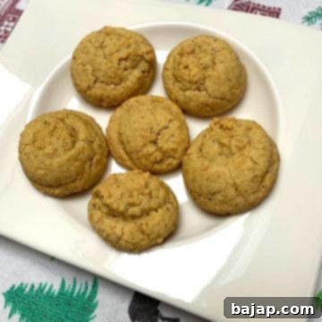 A close-up of golden-brown walnut cookies, made from leftover egg yolks, on a cooling rack, some topped with a whole walnut.