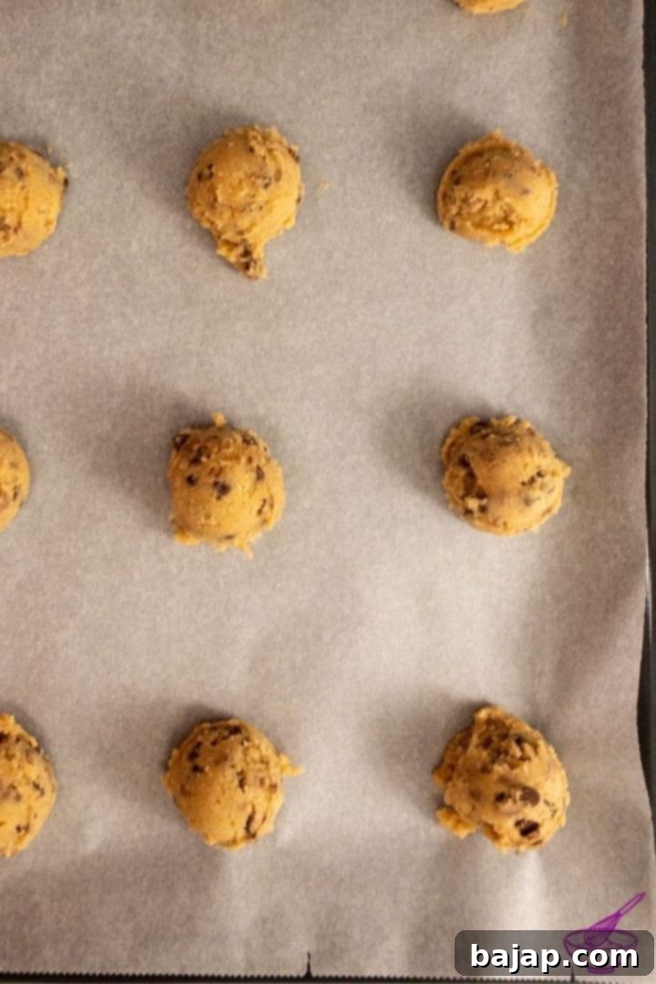 Scooped chocolate chip cookie dough balls with chestnut flour on a parchment-lined baking sheet, ready for baking