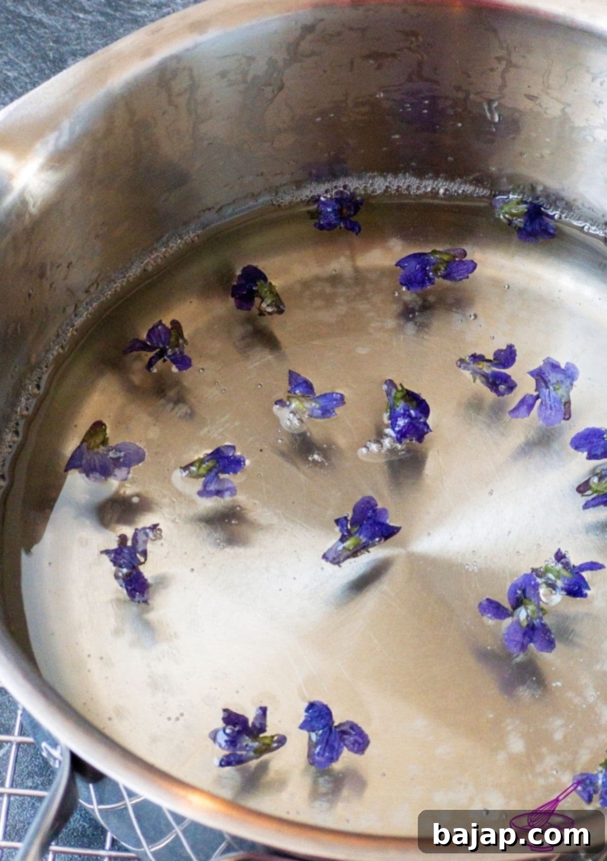 Fresh violets being placed into a sugar solution in a clear bowl.