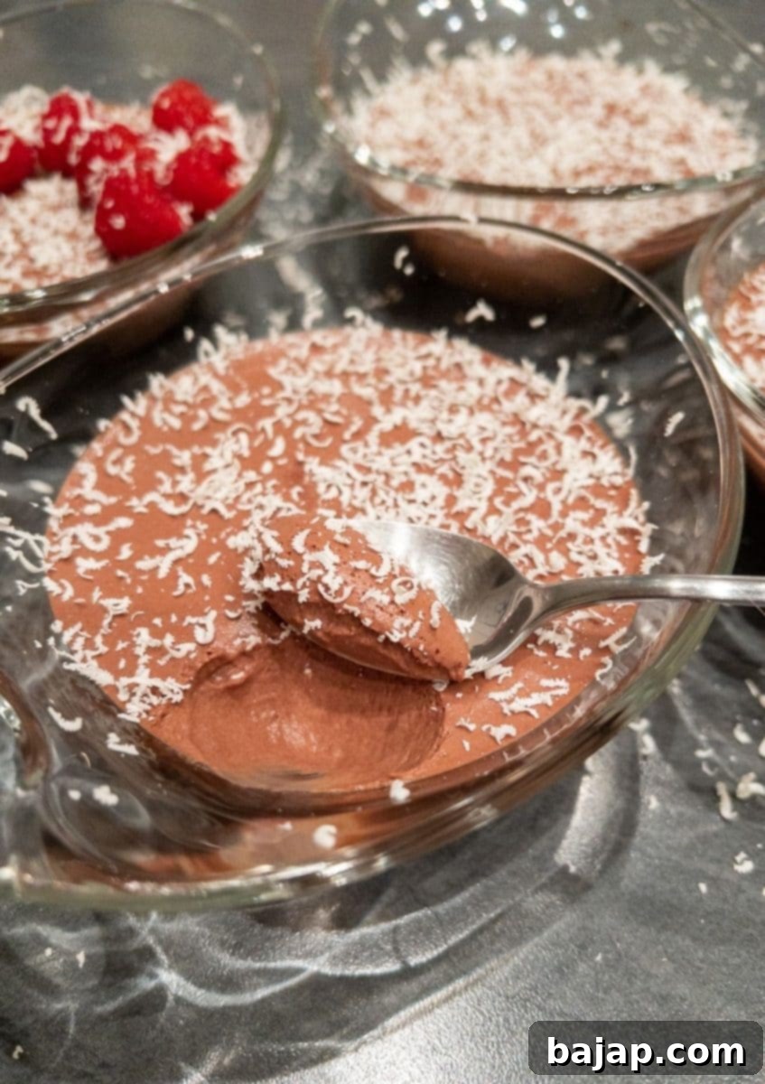 Two glasses of dark chocolate mousse, one topped with fresh raspberries and the other with white chocolate shavings, showcasing its versatility and rich texture.